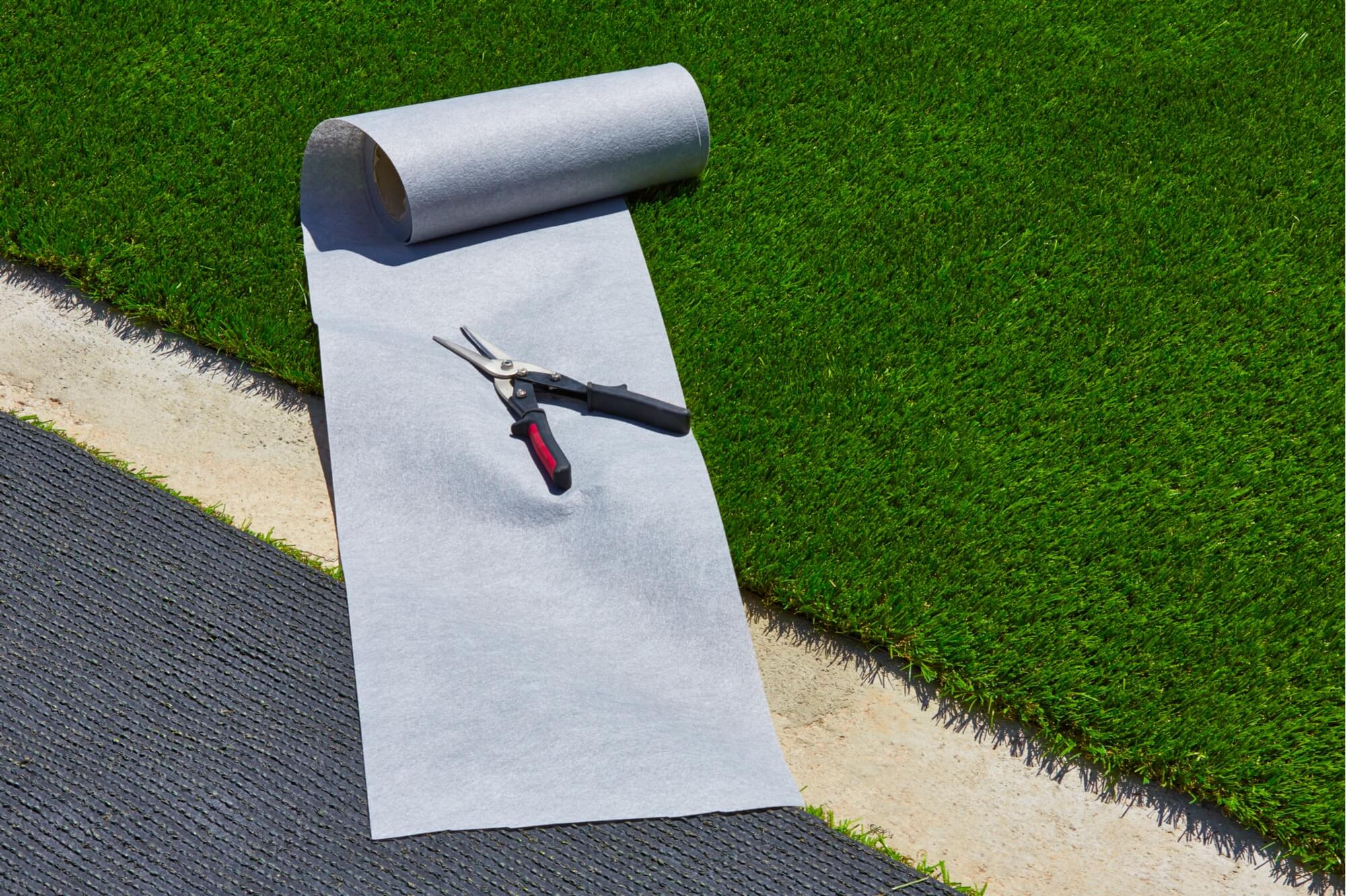 A roll of artificial turf grass laid out on a lawn, with a pair of shears 