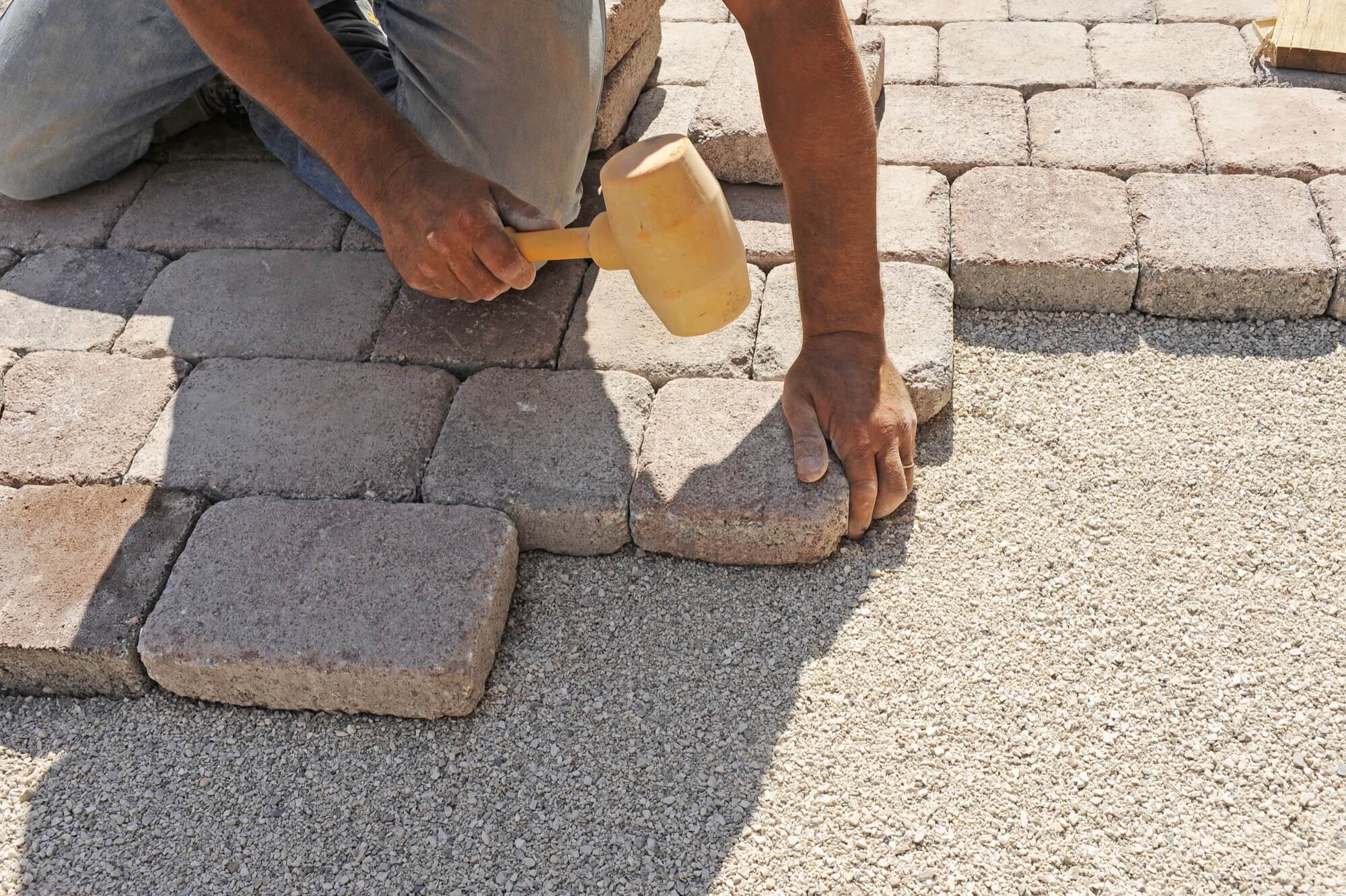 A worker laying down concrete pavers in a driveway.