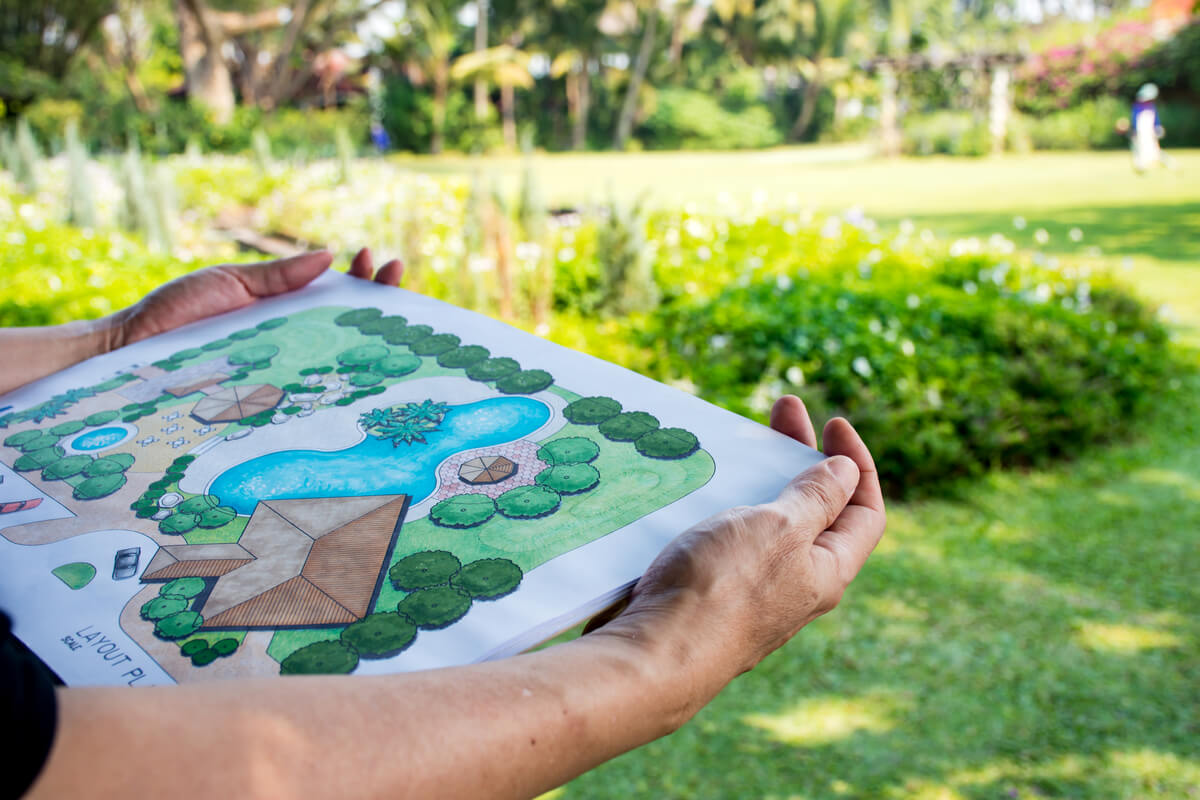 A person holding a landscape design plan in a garden.