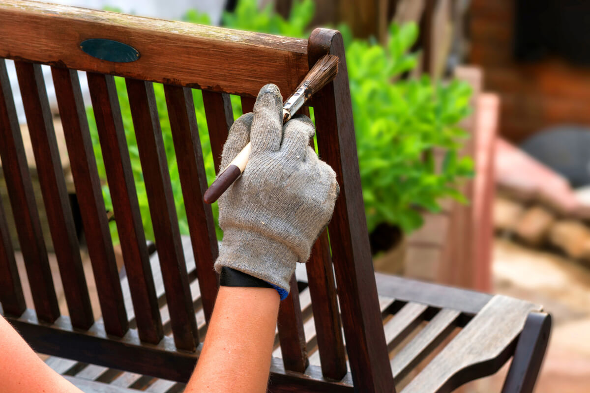 A person painting a wooden chair in patio with a brown paintbrush