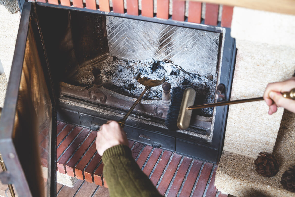 A person cleaning a fireplace with a brush and shovel